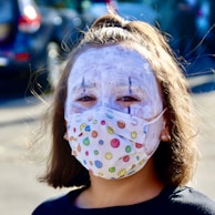 A smiling person wearing a facemask outdoors on a sunny day.