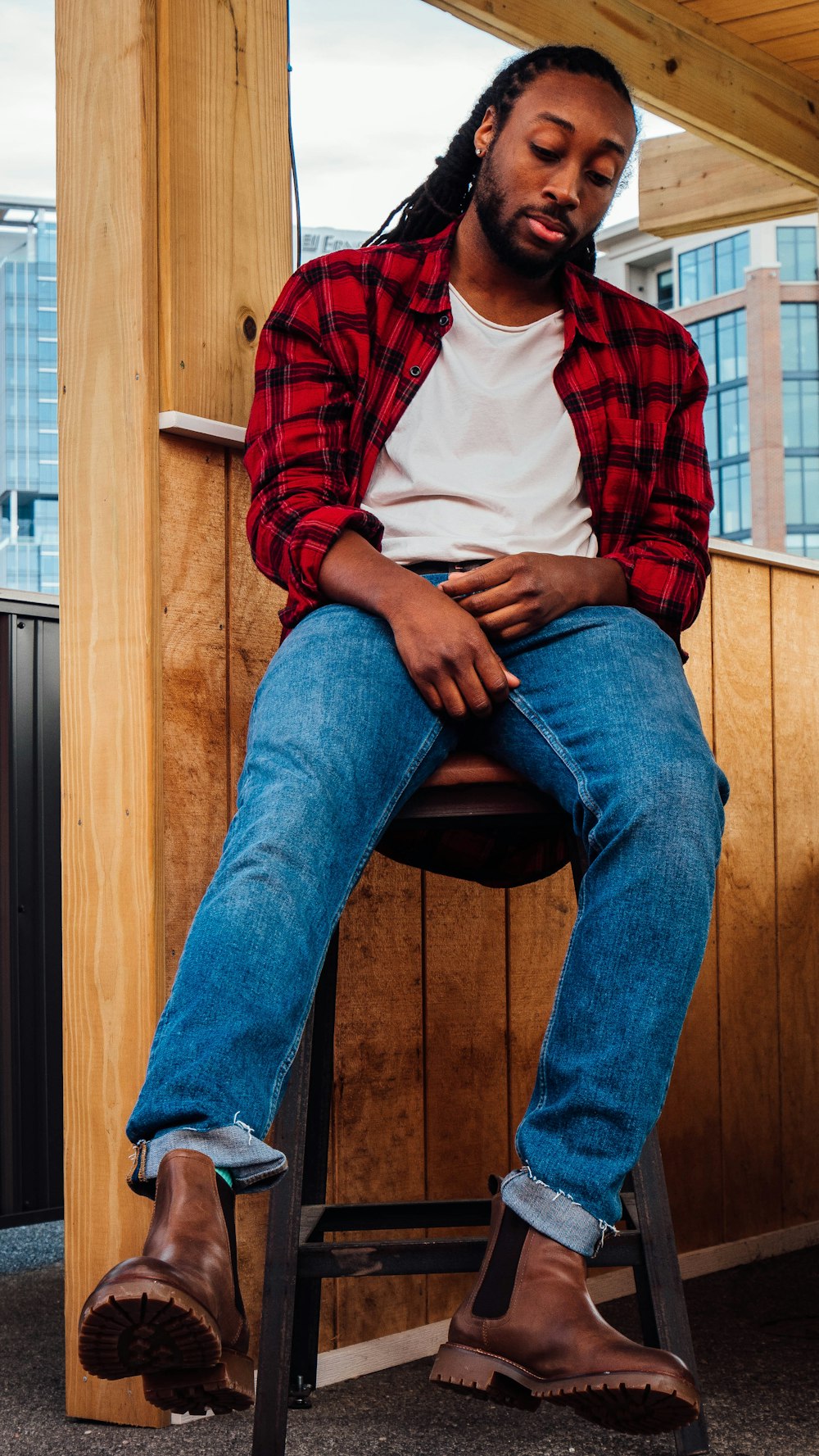 Man in red and white plaid dress shirt and blue denim jeans sitting on  brown wooden photo – Free Model Image on Unsplash