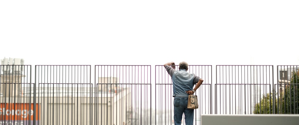 man in blue denim jacket and brown pants standing beside black metal fence