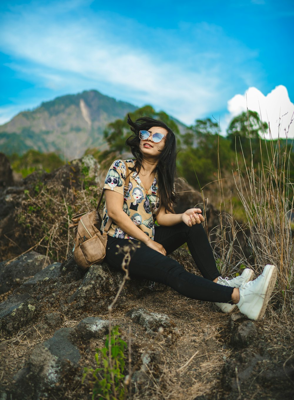 woman in black and white floral shirt and black pants sitting on rock during daytime