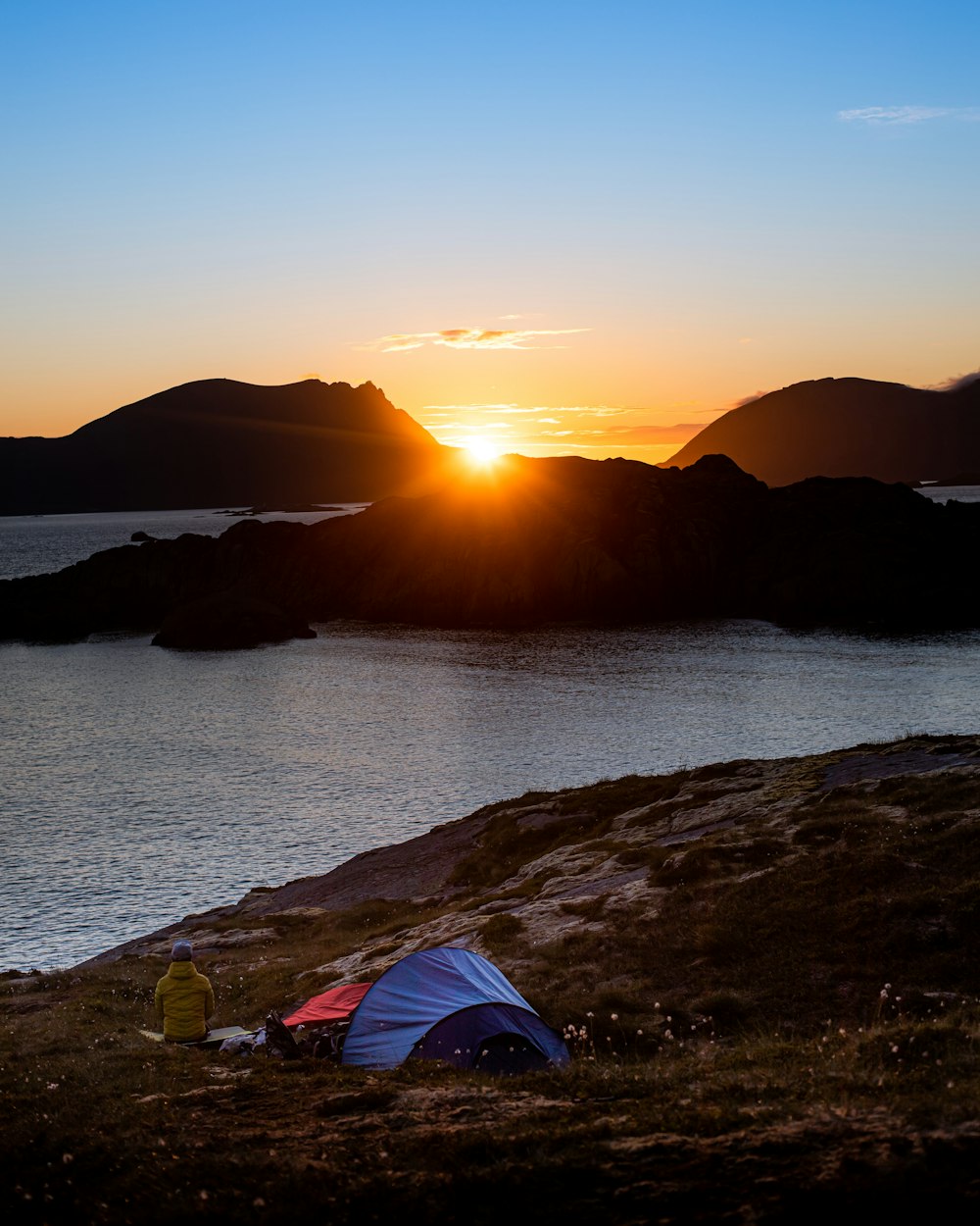 blue and red tent on brown rock near body of water during sunset