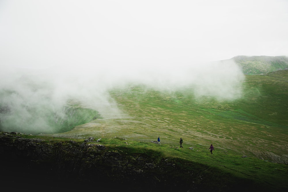 people standing on green grass field near green mountain covered with fog during daytime