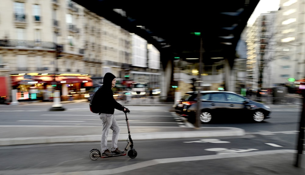 man in black jacket riding on kick scooter on road during daytime