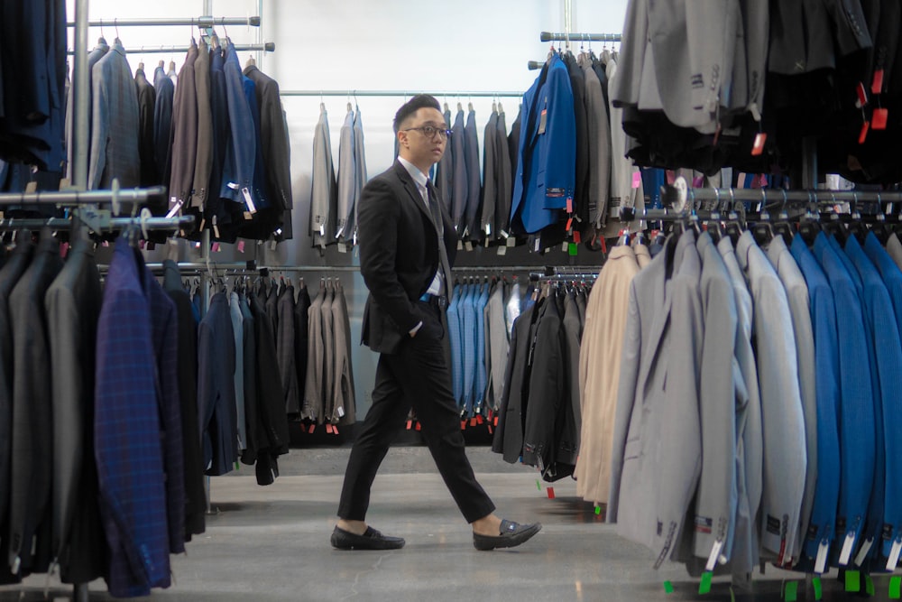 man in gray suit standing near clothes hanged on rack
