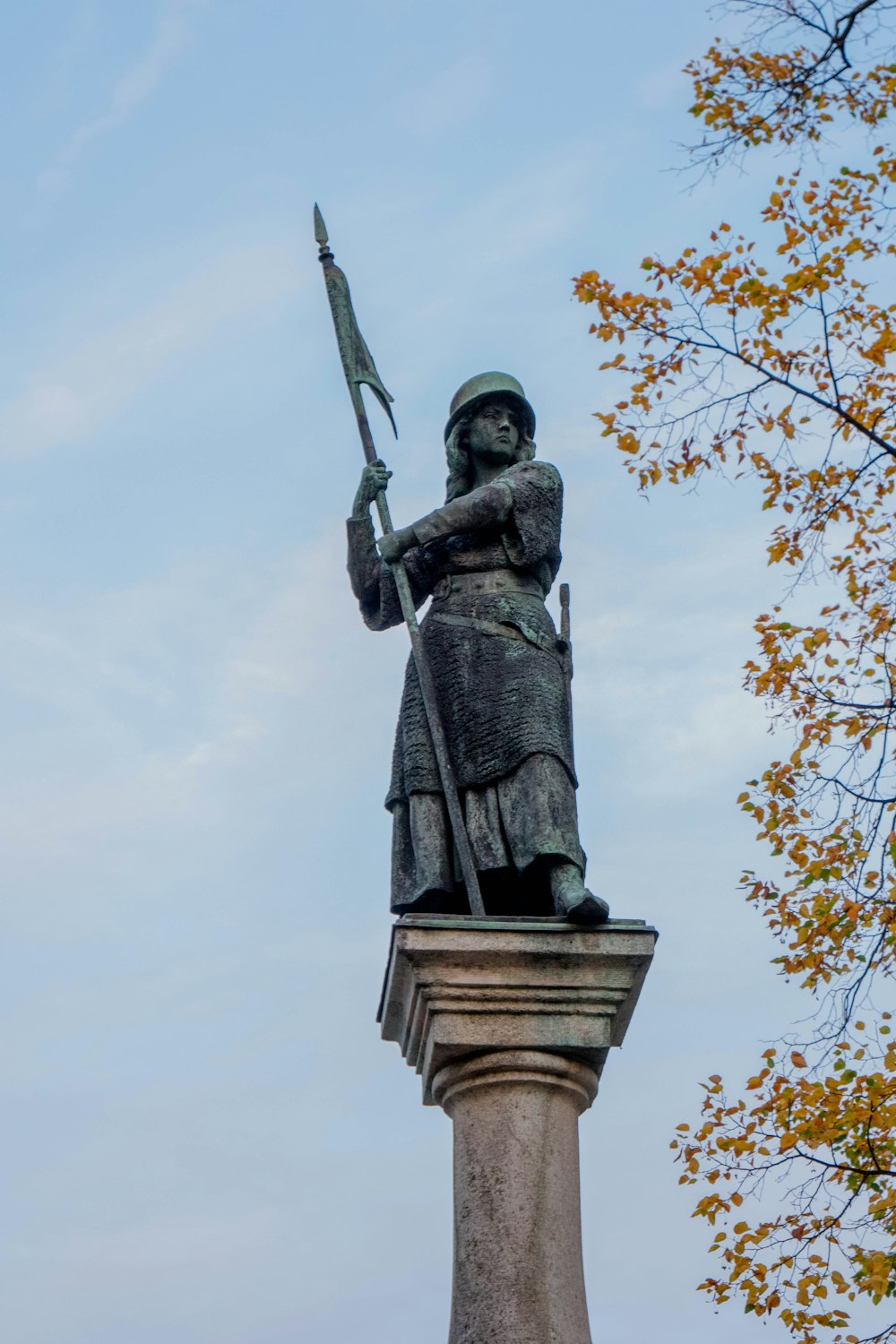 statue of man holding book under white clouds during daytime