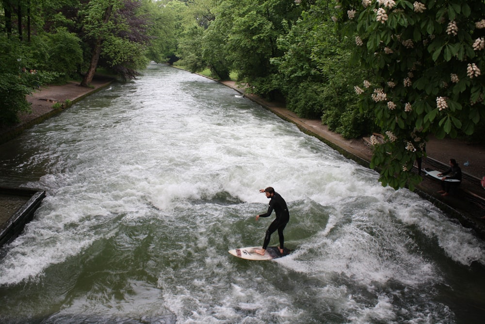 man in black wet suit riding on brown surfboard on river during daytime