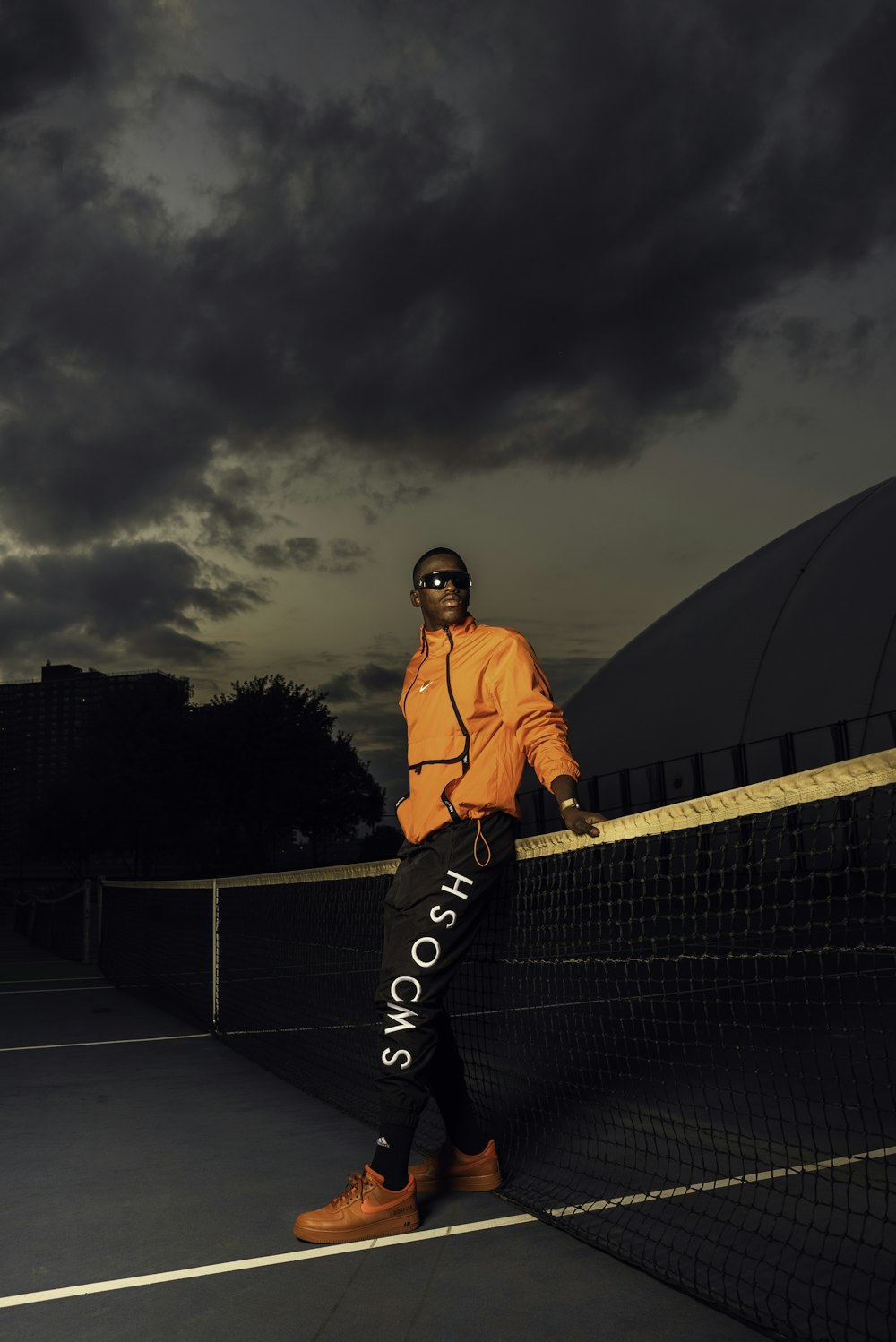 man in orange jacket standing on black metal fence during night time