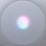 A circular, mesh-covered electronic device with a glowing light centered on the surface, displaying a gradient of colors including pink, blue, and white.