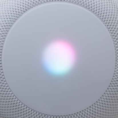 A circular, mesh-covered electronic device with a glowing light centered on the surface, displaying a gradient of colors including pink, blue, and white.