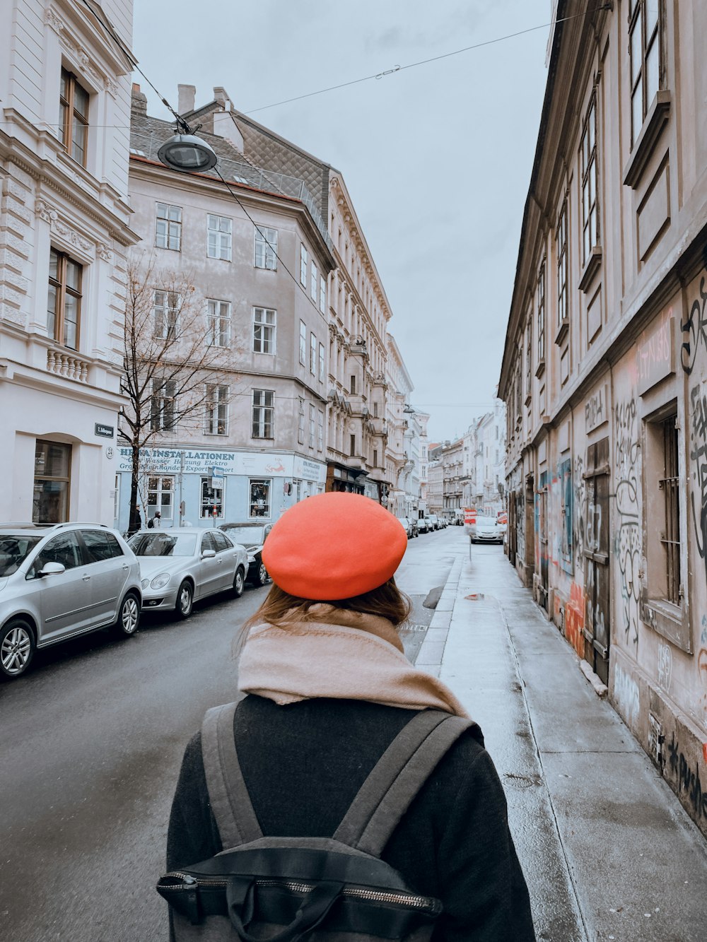 Persona con gorra naranja y chaqueta negra caminando por la acera durante el día