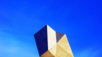 A modern geometric architectural structure with a combination of gold and black colors stands against a clear blue sky.
