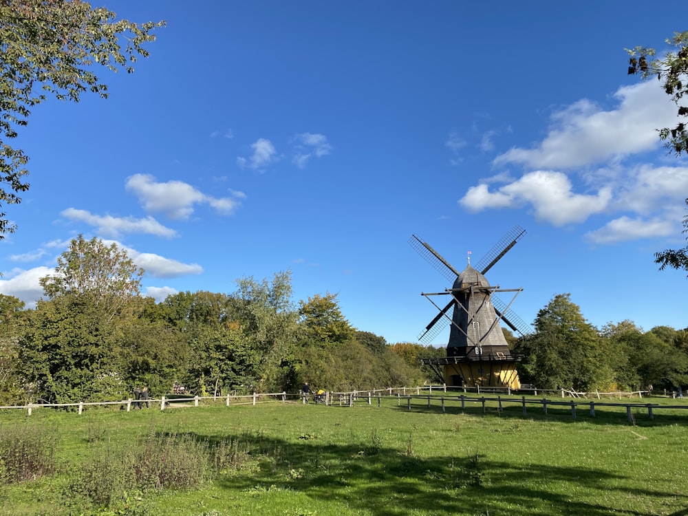 Braune Windmühle auf grünem Grasfeld unter blauem Himmel tagsüber