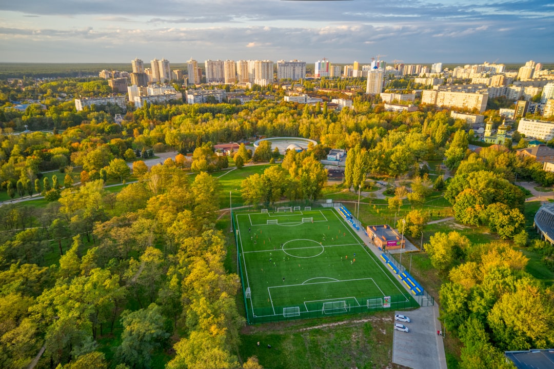 aerial view of green field surrounded by green trees and buildings during daytime