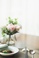 A minimalist table setting with chopsticks, soy sauce dish, and a small vase with a single flower under warm light.