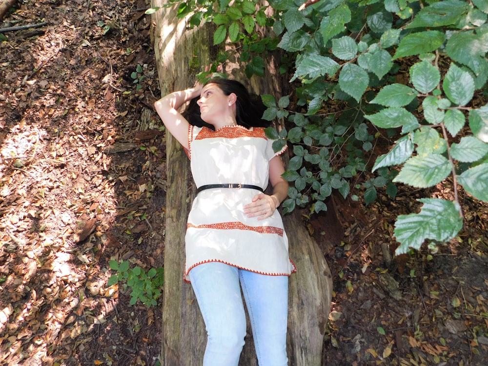 woman in white tank top and blue denim jeans standing beside green leaves