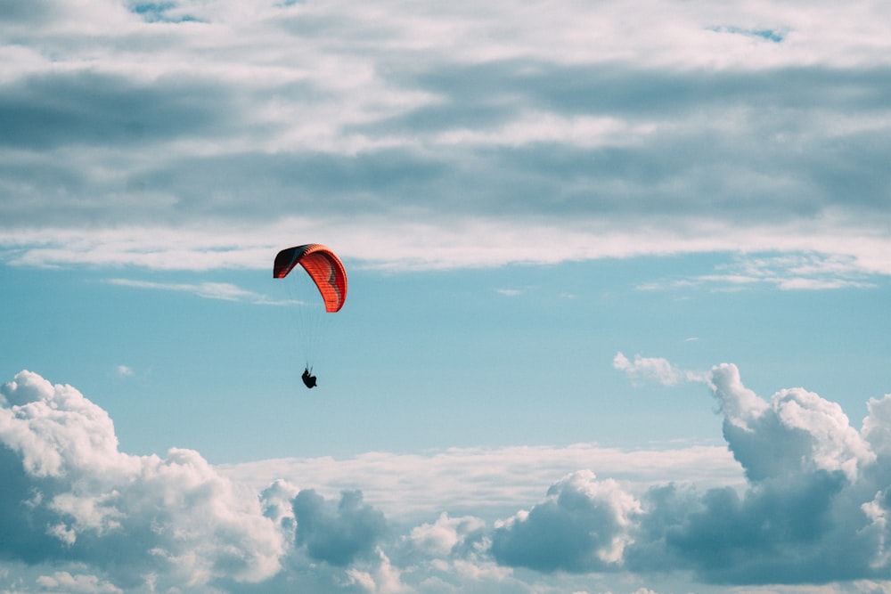 낮 동안 흰 구름 아래 빨간 낙하산을 탄 사람