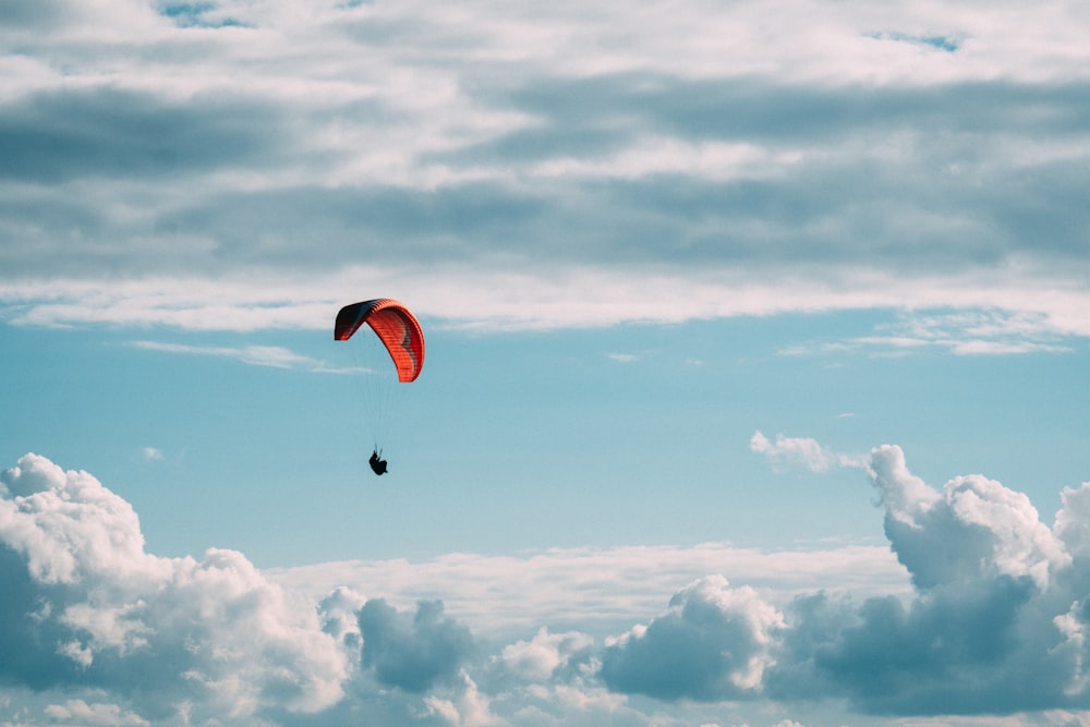 person in red parachute under white clouds during daytime