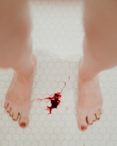 woman standing up and menstruating on white ceramic floor tiles