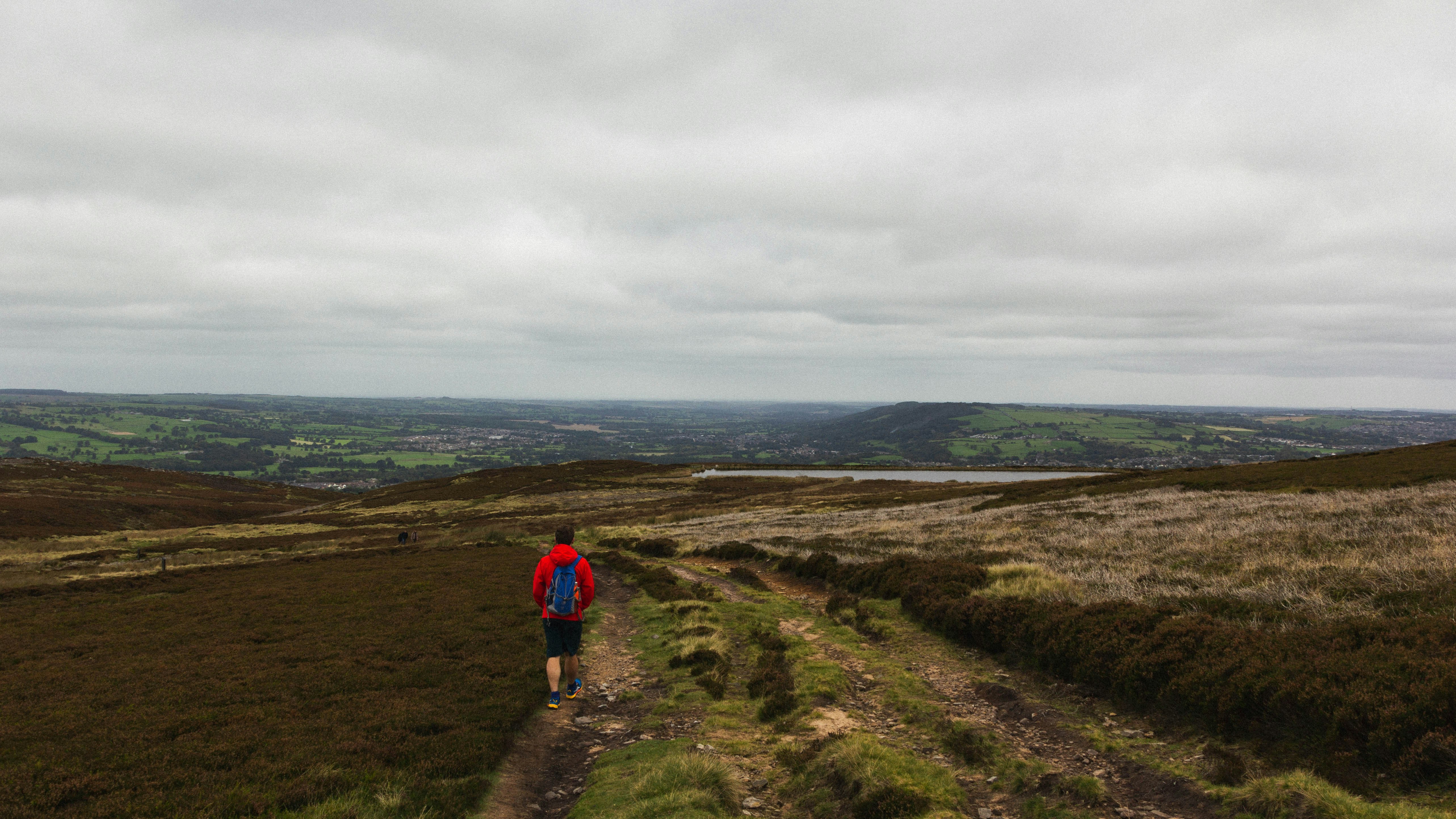 person in red jacket walking on green grass field under white cloudy sky during daytime