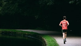 A smiling person jogging outdoors surrounded by greenery.