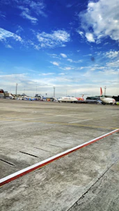 An airport runway with a cargo plane being loaded under a bright sky.