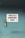 A teal brick wall features a prominent white sign that reads 'This is a SMOKING AREA' in bold black letters. Below the text are graphic symbols of cigarettes indicating permitted smoking. An ashtray is mounted on the wall to the left of the sign, used to dispose of cigarette butts.