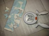 A butterfly-shaped paper punch is lying on a textured silver surface next to a strip of paper with cloud patterns. The paper has several butterfly-shaped cutouts, and a few of these cutouts are placed nearby on the surface.