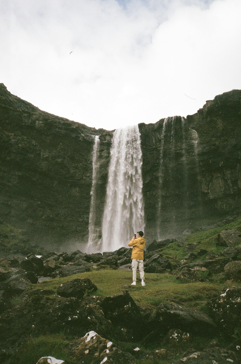 person in yellow jacket standing on green grass field near waterfalls during daytime