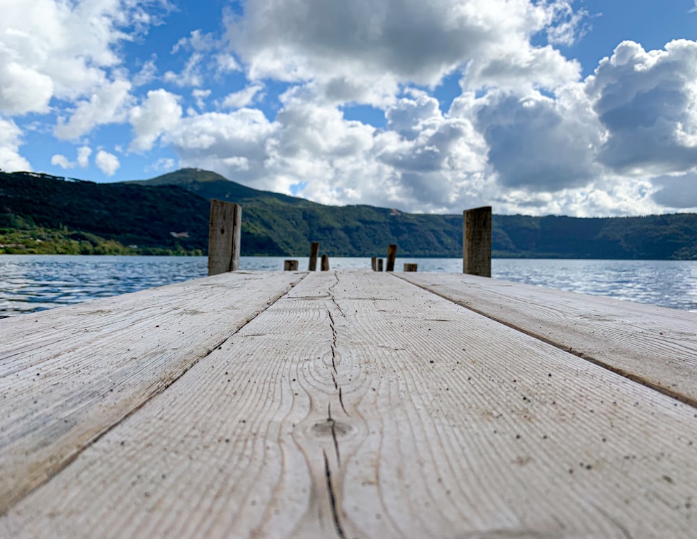 brown wooden dock on body of water under white clouds and blue sky during daytime