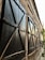 A row of large, closed wooden shutters with a lattice design, mounted on an old building with a textured stone facade. The shutters are painted black and secured with metal braces, and the setting appears to be a narrow alley with soft evening light reflecting off the windows.