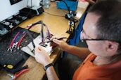 a man in an electronics shop holding soldering iron performing repairs on a printed circuit board