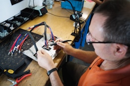 a man in an electronics shop holding soldering iron performing repairs on a printed circuit board
