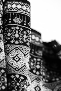 Detailed black and white close-up of a richly patterned knitted fabric with an intricate design that includes geometric shapes and symmetrical motifs.