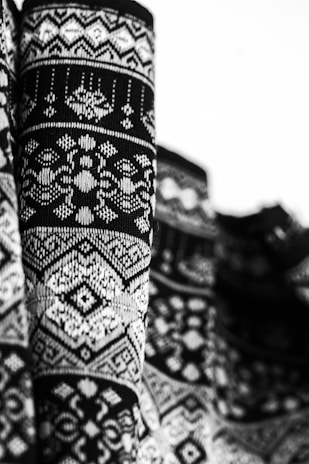 Detailed black and white close-up of a richly patterned knitted fabric with an intricate design that includes geometric shapes and symmetrical motifs.