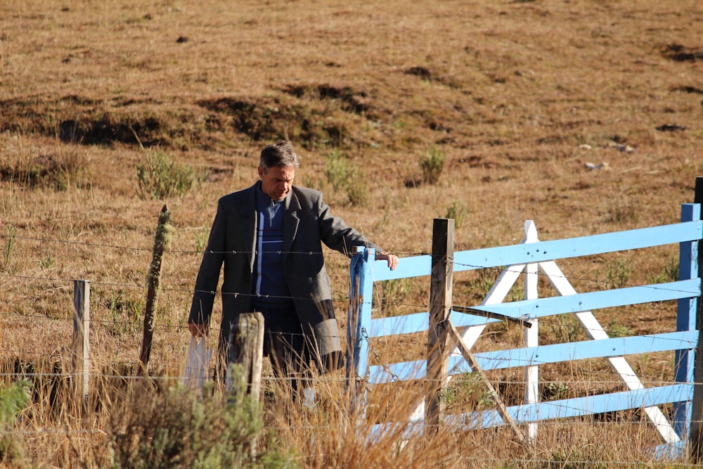 man in black suit standing beside white wooden fence during daytime