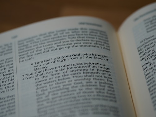 A close-up view of an open book, with visible text written in English. The focus is on the middle section where specific verses are highlighted, mentioning God and religious commandments.