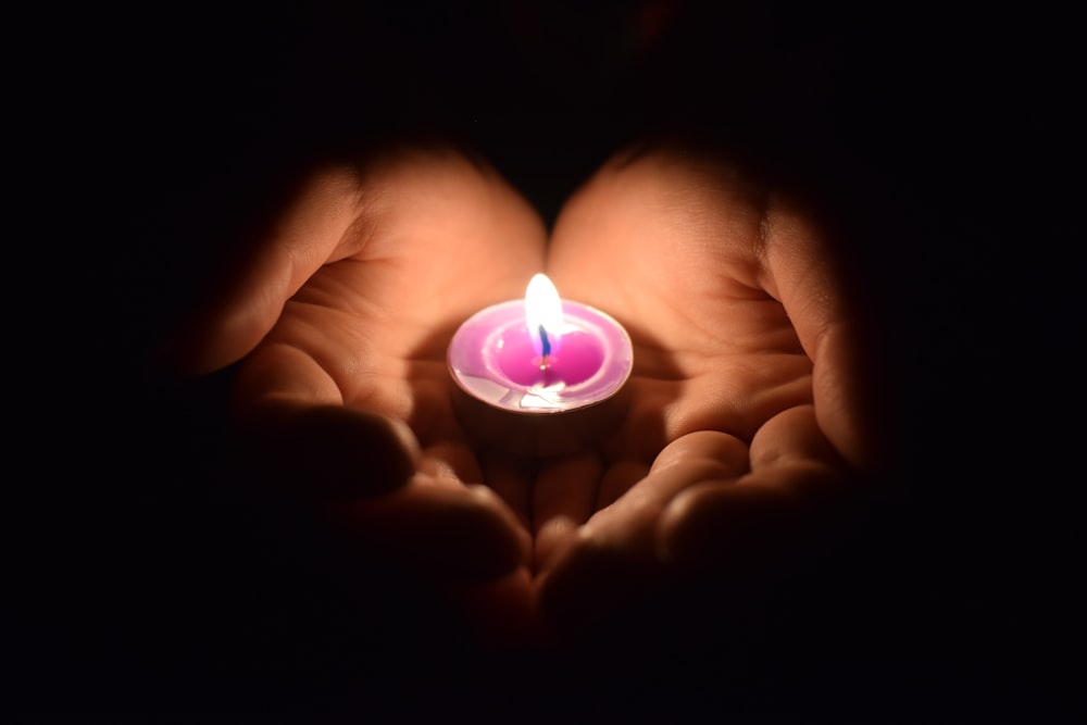 person holding lighted candle in dark room