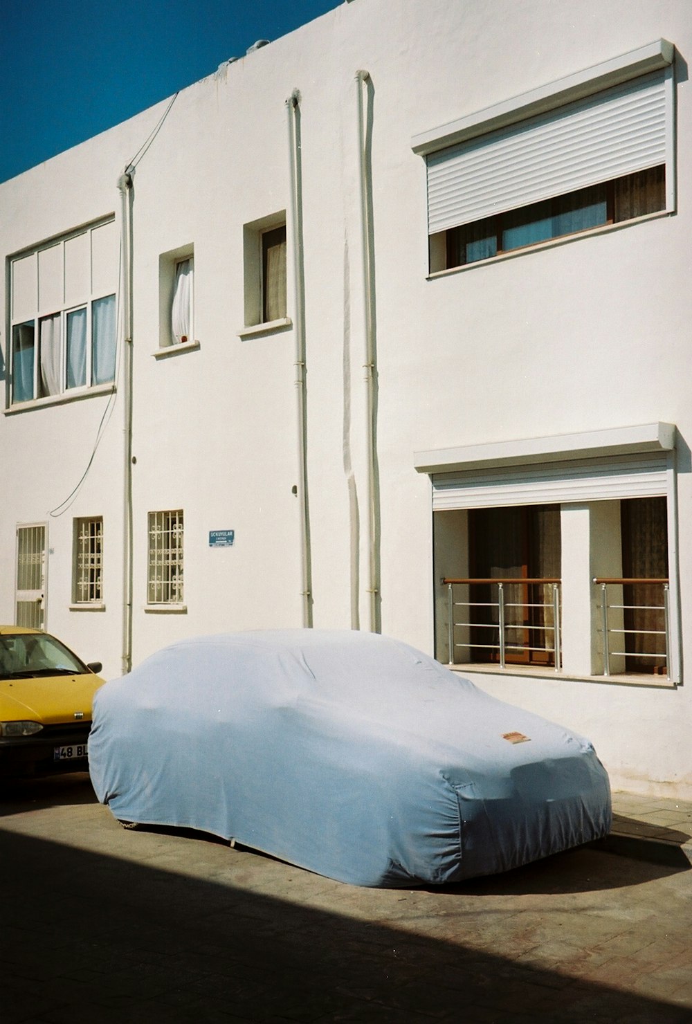 Auto gialla parcheggiata accanto all'edificio in cemento bianco durante il giorno