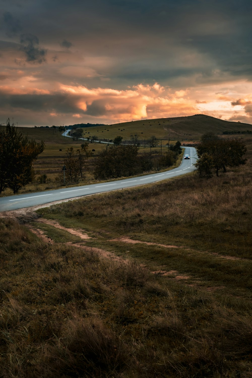 gray road between green grass field during daytime