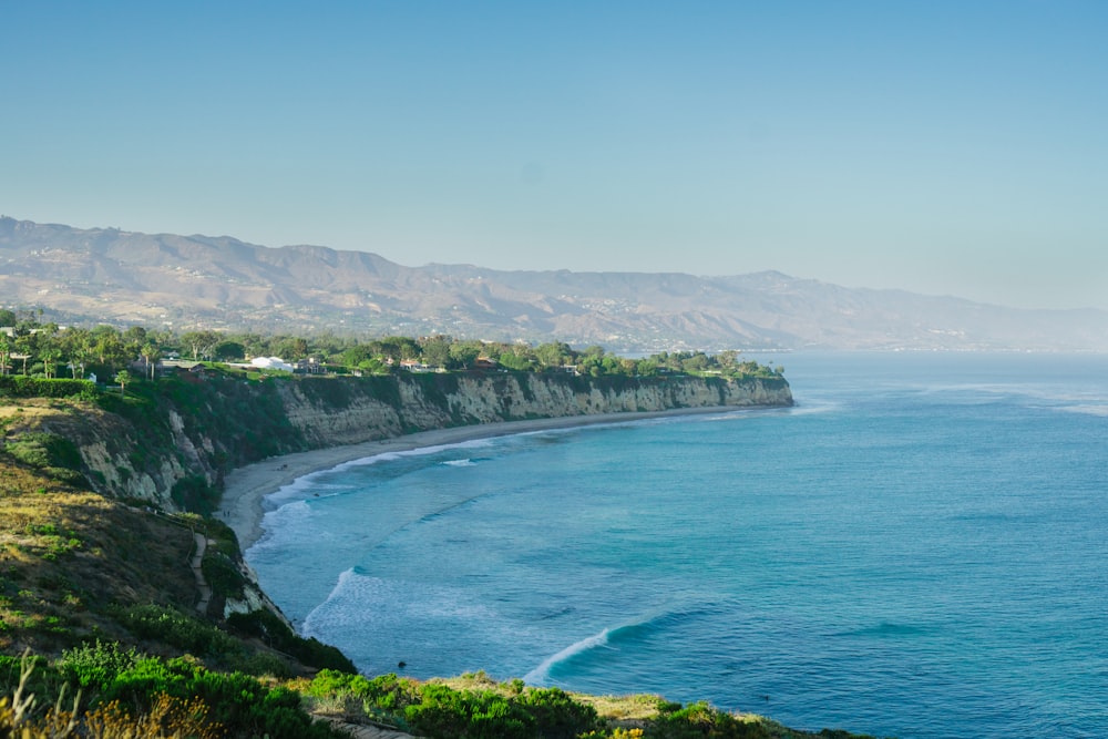 árvores verdes na montanha ao lado do mar azul sob o céu azul durante o dia