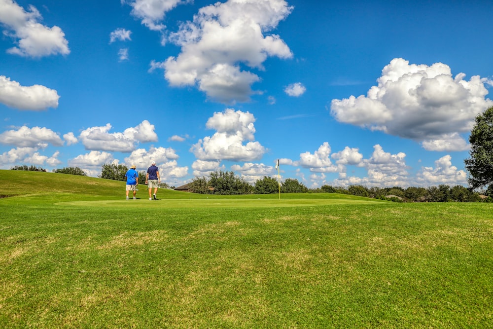 people playing golf on green grass field under blue and white cloudy sky during daytime