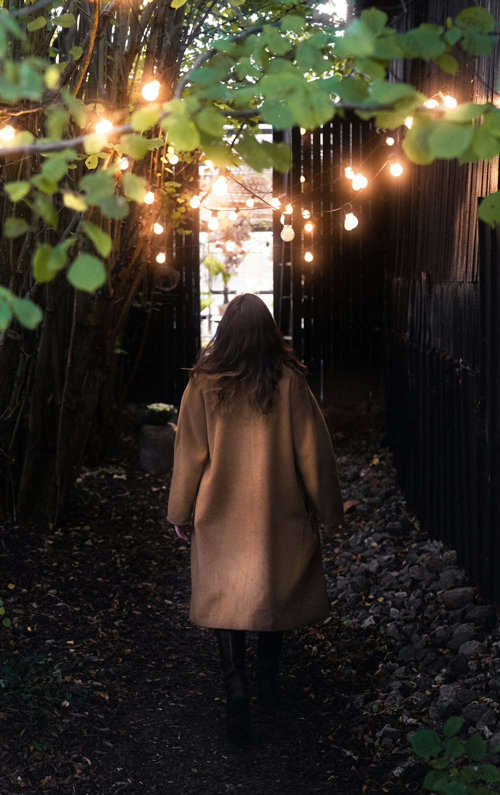 woman in brown coat standing near brown wooden fence during night time