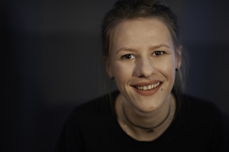 A warm, inviting portrait of the piercing artist smiling in the pastel purple and yellow studio.