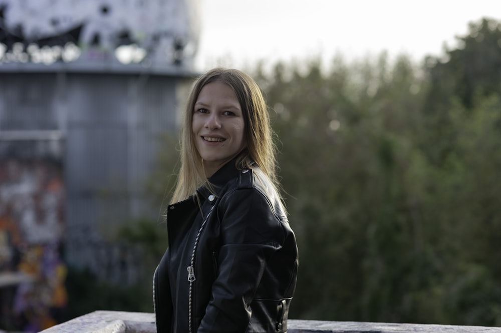 woman in black leather jacket standing near body of water during daytime