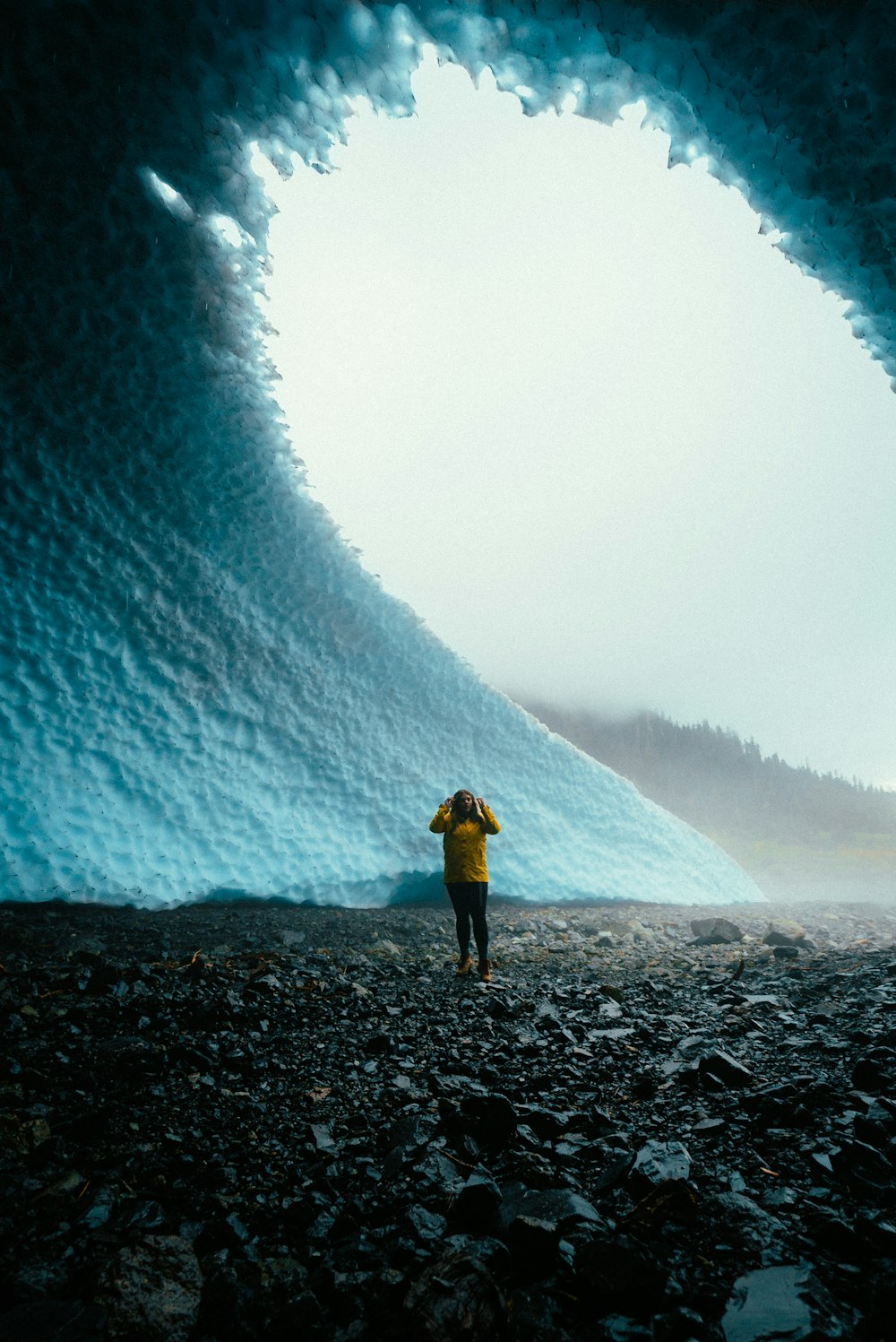 person in yellow jacket and black pants standing on rocky ground during daytime