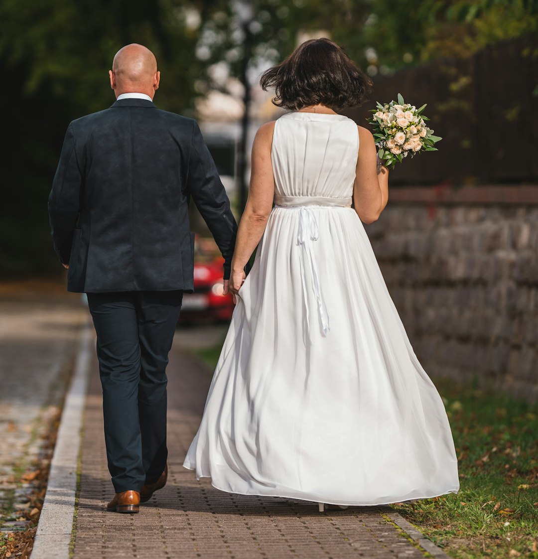 man in black suit and woman in white wedding dress walking on sidewalk during daytime