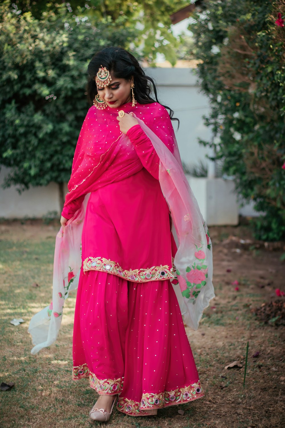 woman in pink and red sari standing on green grass field during daytime