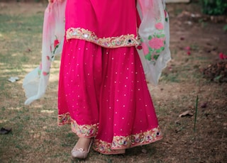 woman in pink and red sari standing on green grass field during daytime