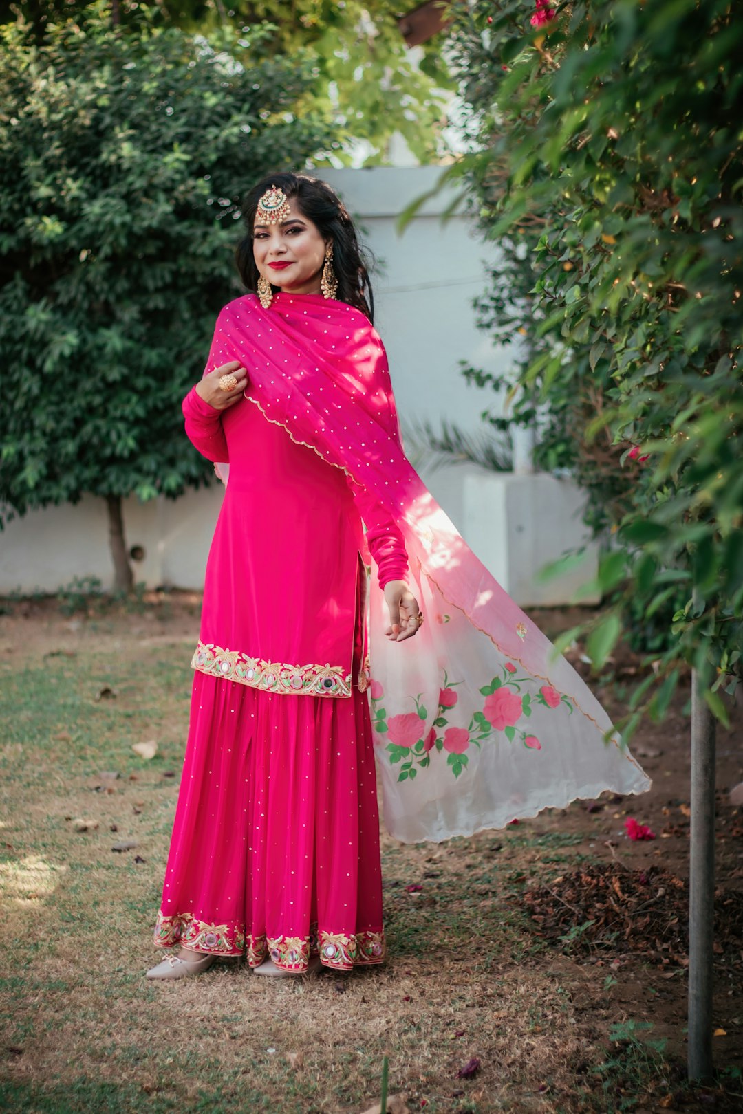 woman in red and white sari standing on green grass field during daytime