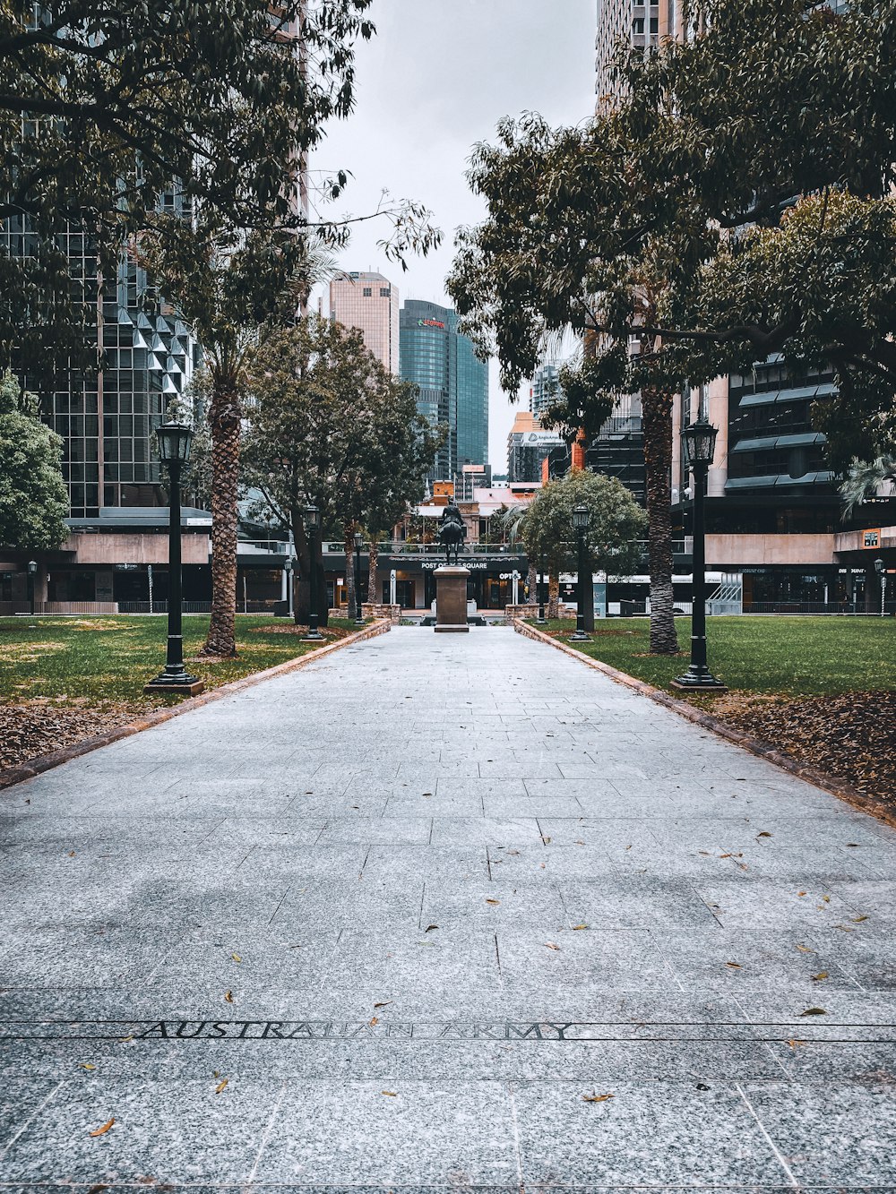 gray concrete pathway between green trees and brown wooden bench during daytime